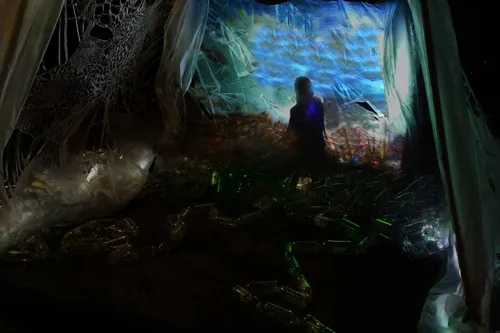 A plastic projection screen created with translucent plastic waste materials such as beverage bottles, shower curtains, food containers wraps 3 sides of a tent. installation view